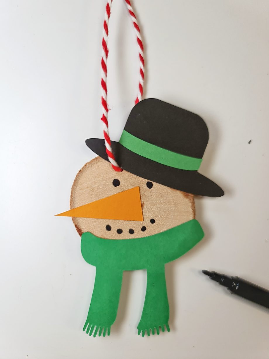 Snemand fra kreasættet med juleophæng. Snemanden har grønt tørklæde og sort hat. Lavet af træskive og karton.
