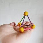 Hånd holder en 3d geometri trekant lavet af kugler af gul modellervoks og farvede træpinde