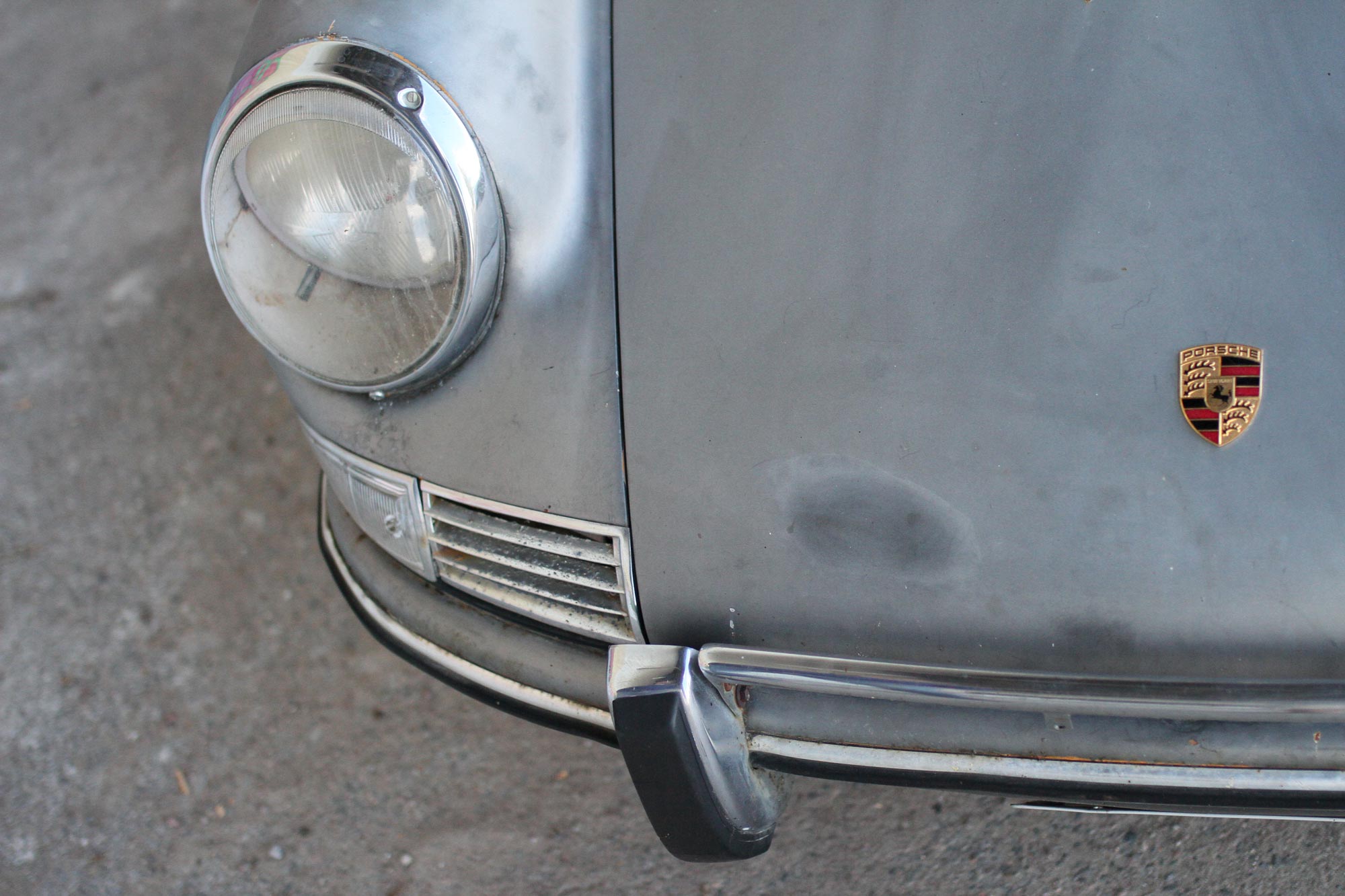 The Porsche badge in the front of the car together with the headlights on a patina 912