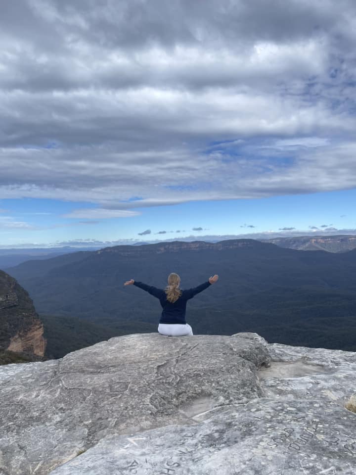 Sydney Blue Mountains. Kathrine sidder på klippekanten og nyder udsigten. Hun sidder med armene ud til siden og omfavner verden.