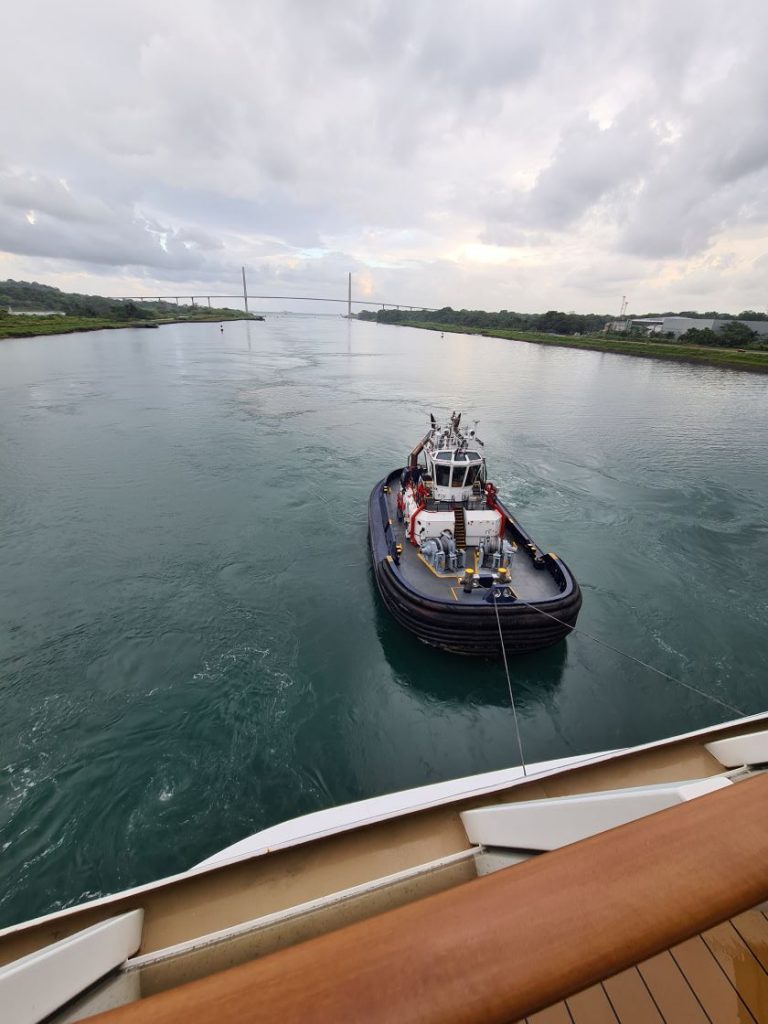 En slæbebåd finder sin position ved agter enden af skibet. Puente Atlantico ses langt bagude