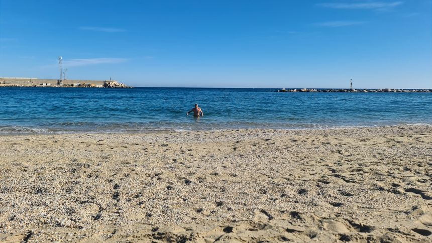 Rejseblog. Garrucha, Spanien – Fiskerby, fest og hverdag. Søren bader ved stranden ved havnen. I baggrunden molen med sand til afhentning af de store skibe