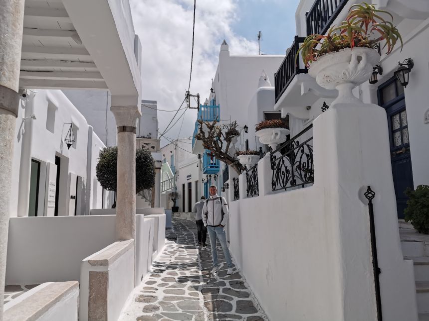 En smal gade i Mykonos by med lyseblå skodder og stenbelægning med hvide fuger