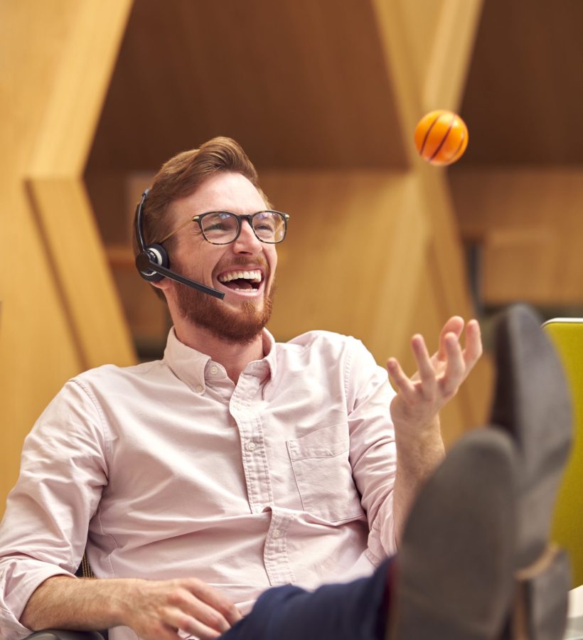 Businessman Wearing Headset Playing With Stress Ball Talking To Caller In Customer Services Centre