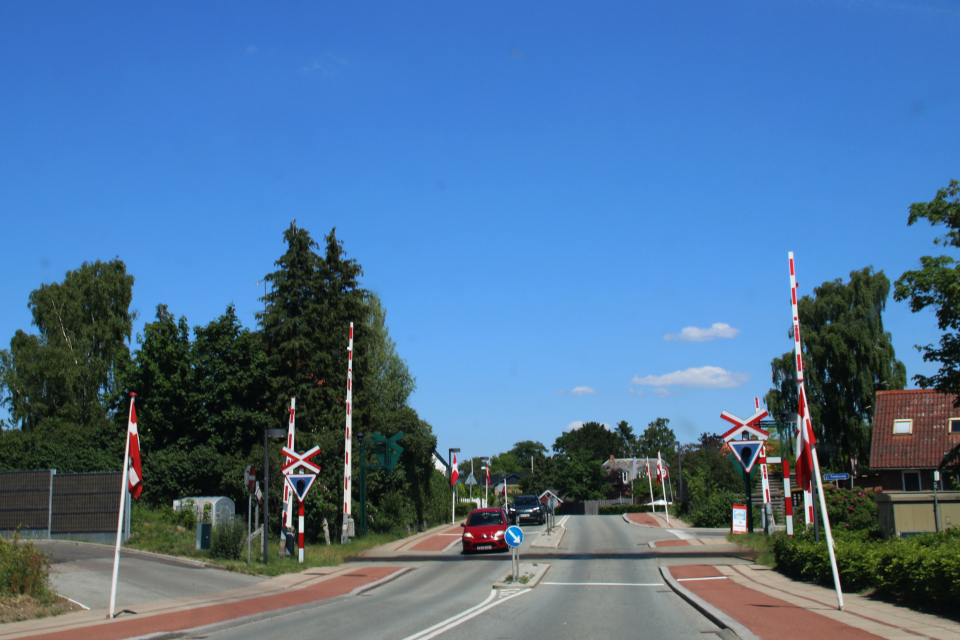 Датские флаги вдоль дороги, проходящей через железнодорожный переезд