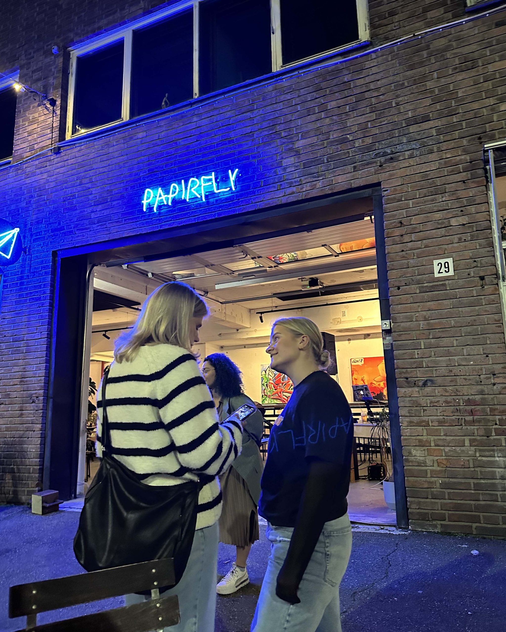 Kveldsbilde fra inngangspartiet til Papirfly bar med mennesker som prater utenfor