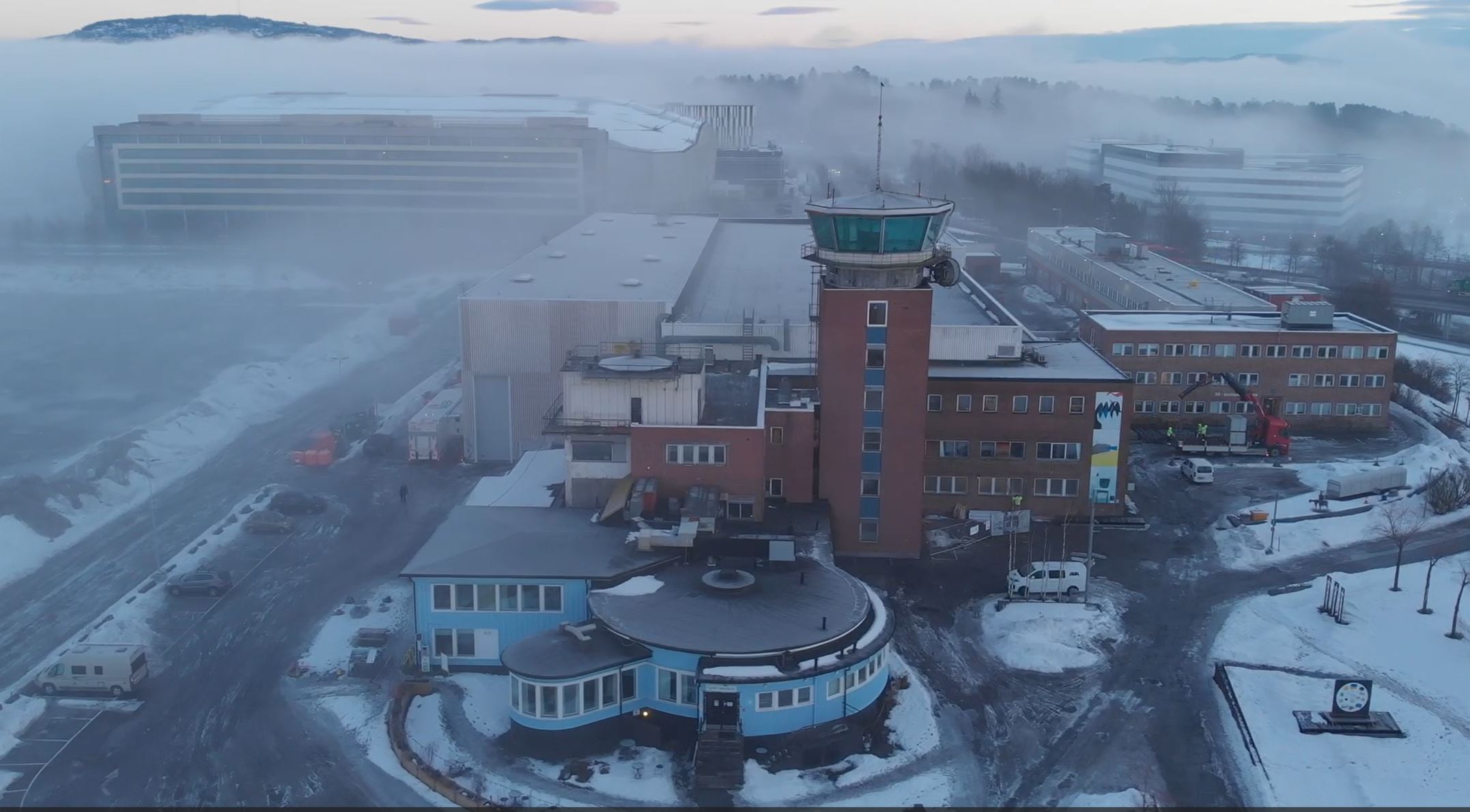 Dronebilde av Flytårnet Fornebu og snødekte omgivelser badet i frostrøyk