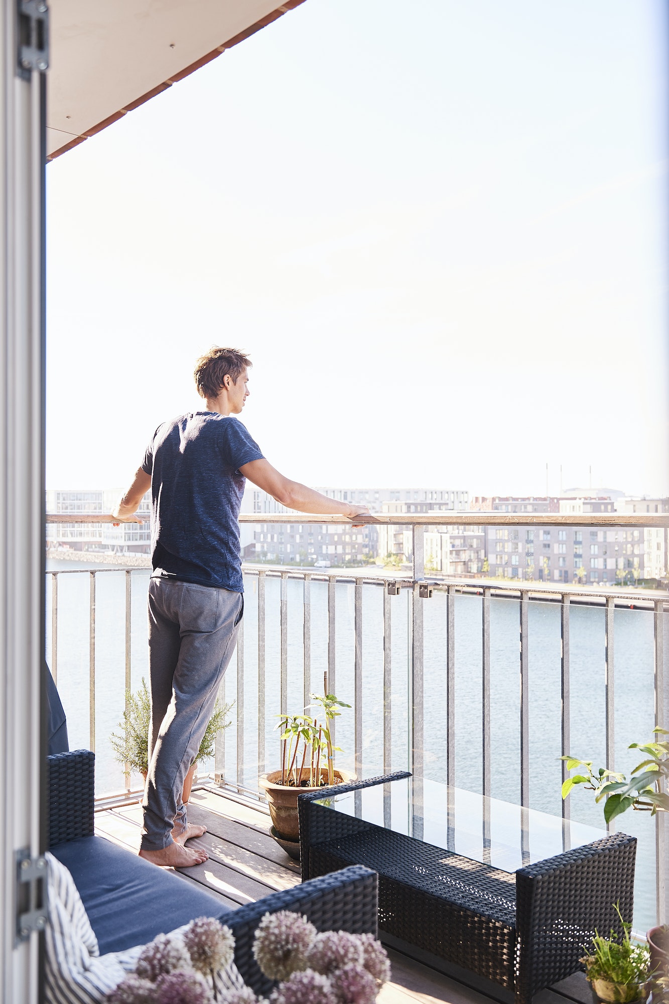 Mid adult man looking out from waterfront apartment balcony