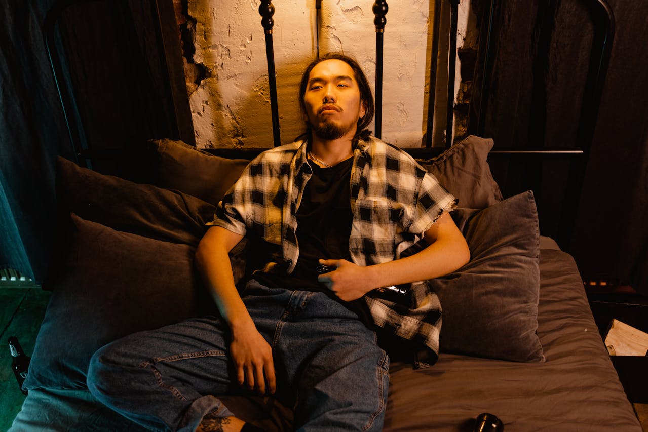 A man in a plaid shirt and jeans lying on a bed looking contemplative and stuck in a masturbation addiction cycle