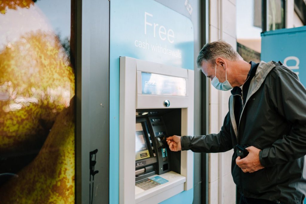 A man at a cash machine wearing a mask, symbolising the pattern of spending associated with being addicted to escorts.