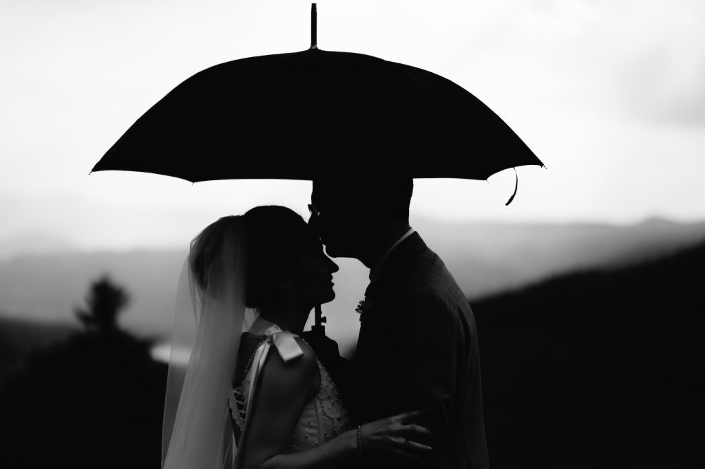 Photo mariage en Belgique noir et blanc. les mariés sont sous un parapluie et s'embrassent