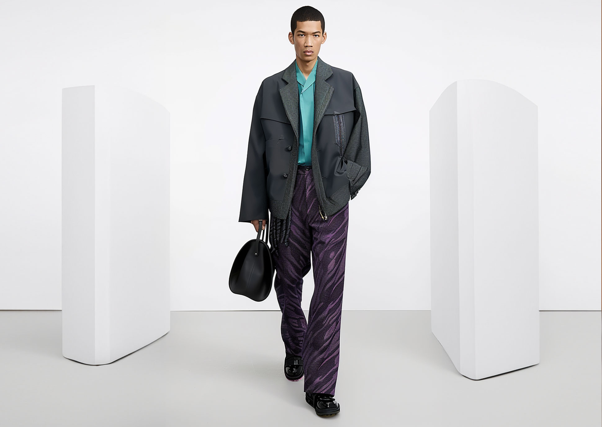 A mixed-race male fashion model walks on a catwalk wearing a grey with purple outfit.