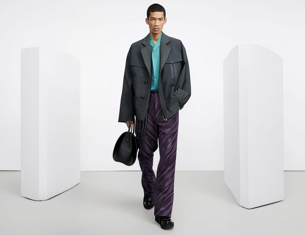 A mixed-race male fashion model walks on a catwalk wearing a grey with purple outfit.