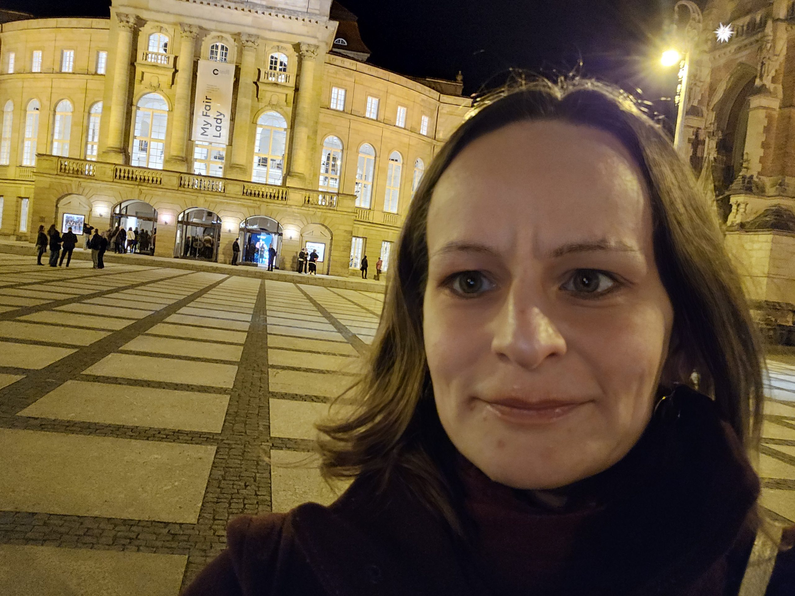 Eine Frau steht vor einem beleuchteten Gebäude mit einem Plakat, auf dem "My Fair Lady" steht