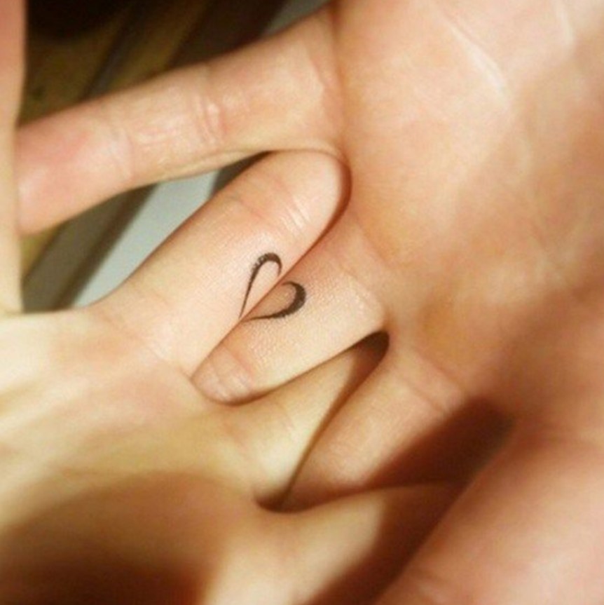 Gemeinsames Herztattoo Zwei miteinander verflochtene Hände, die ein gemeinsames Tattoo in Form eines Herzes haben.