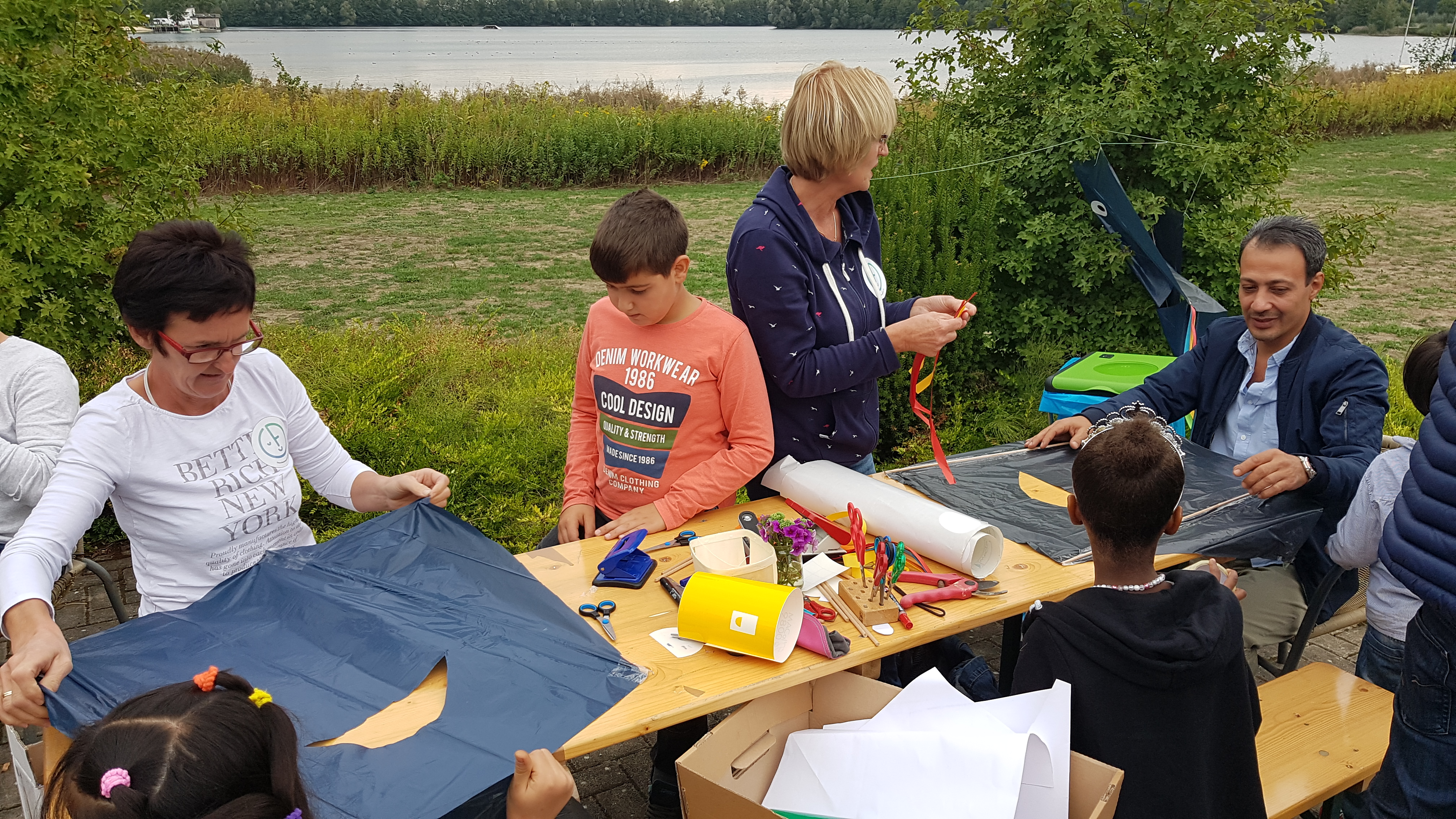 Junge und alte Menschen sitzen und stehen an einem Tisch der mit Bastelutensilien bedeckt ist