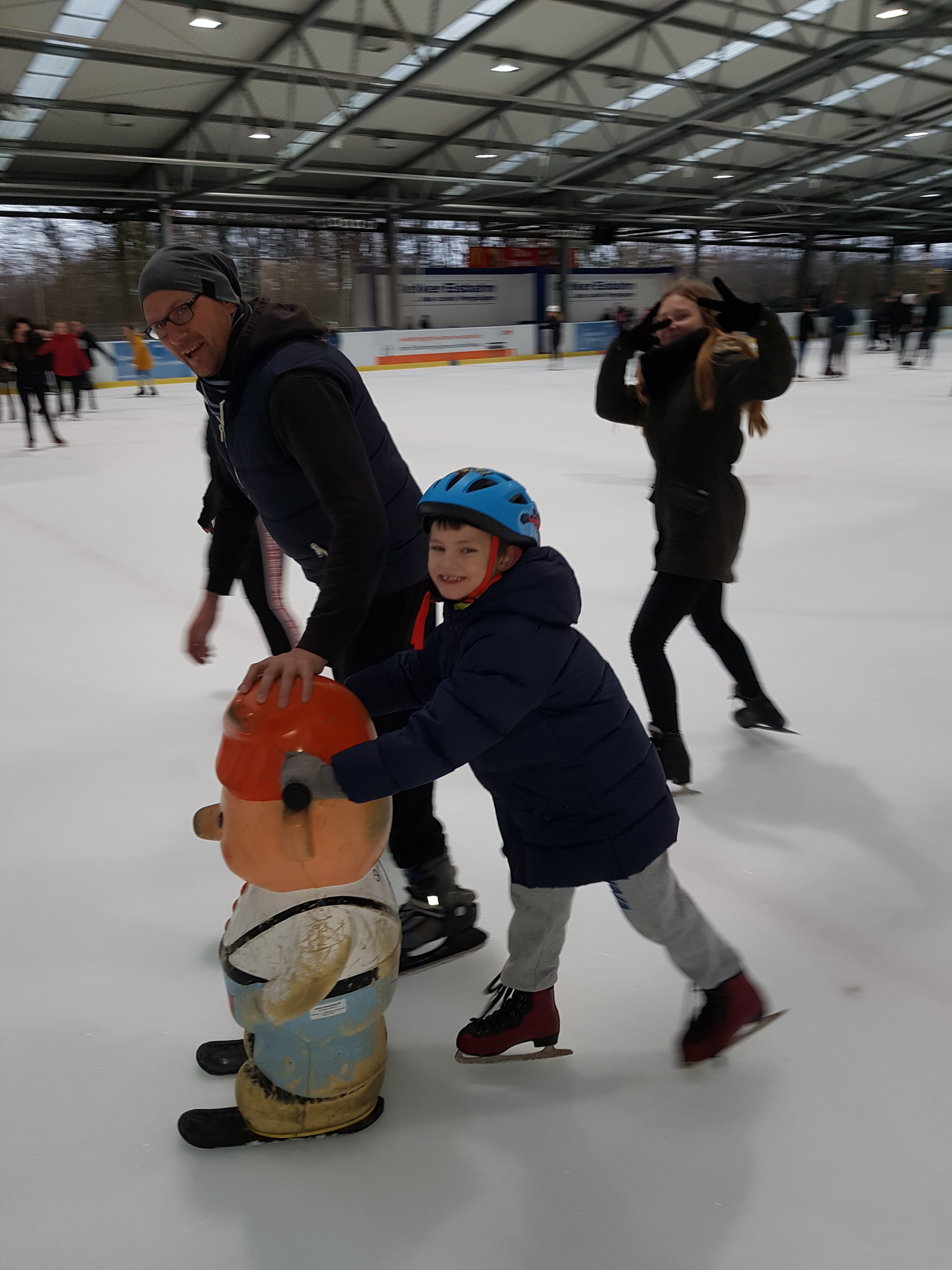 Man sieht drei Menschen, die auf einer Eislaufbahn unterwegs sind