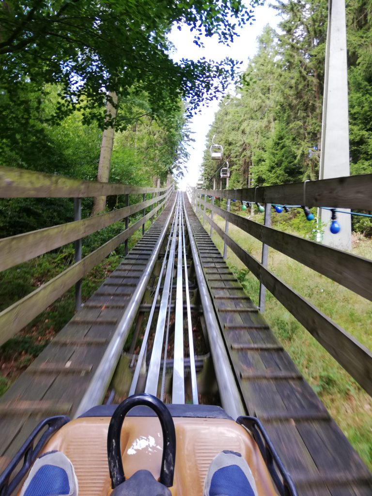 Auf dem Bild sind zwei Füße zu sehen, die in einem Wagen eine Holzachterbahn hinauf fahren.