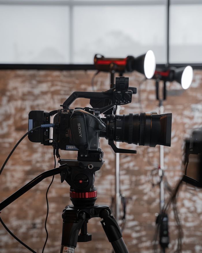 Professional video camera set up in a studio with lighting equipment in background.
