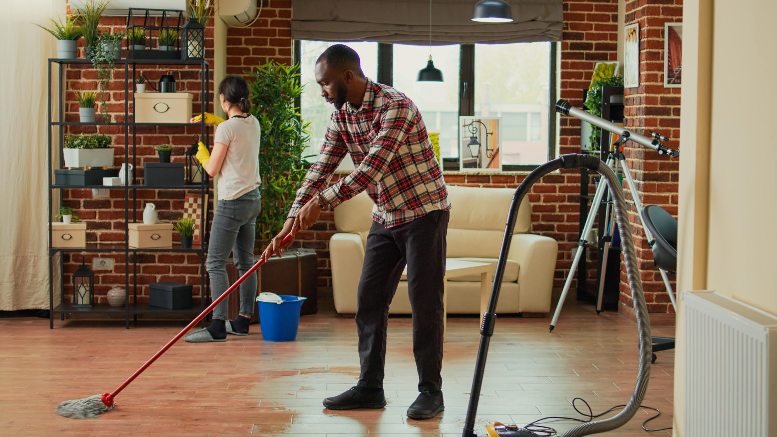 interracial-couple-vacuuming-floors-cleaning-furniture-shelves-sweeping-dust-dirt-with-tools-life-partners-using-vacuum-cleaner-with-hose-gloves-rags-clean-household-house-chores-min