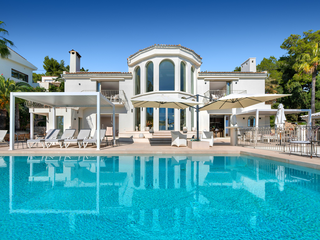 Fachada de una villa con una piscina delante donde se refleja la fachada