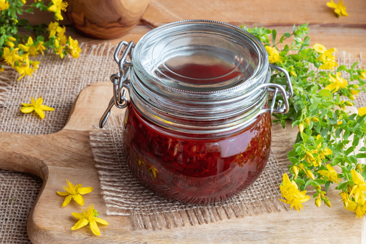 Johanniskrautöl im Glas, dabeben Blüten vom Johanniskraut