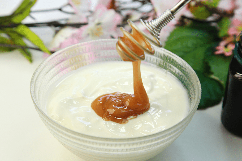 Joghurt und Manuka Honig in Glasschale mit Manuka Blüten im Hintergrund