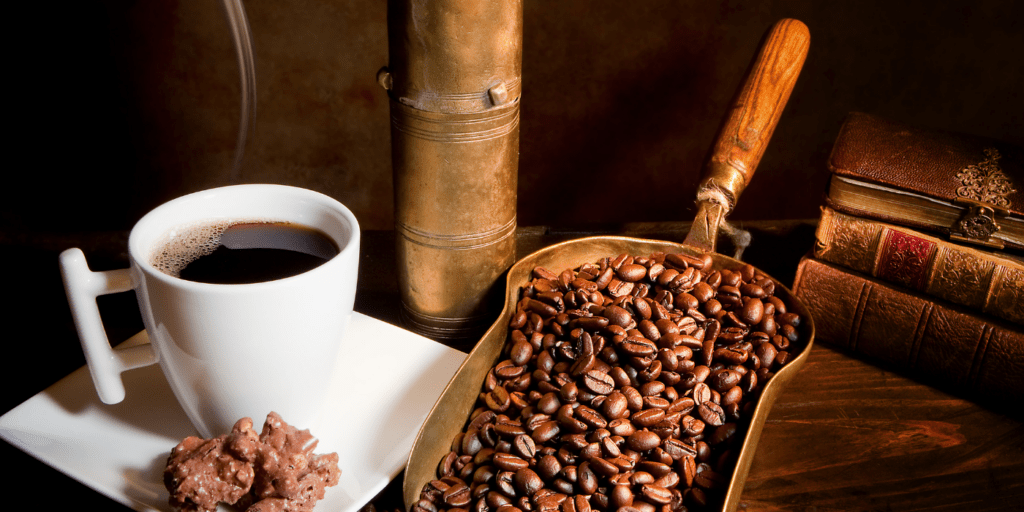 Kaffee in Tasse, daneben Kaffeebohnen auf Messingschaufel