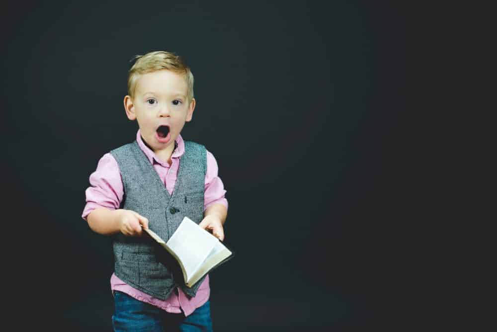 Little boy holding book looking surprised.