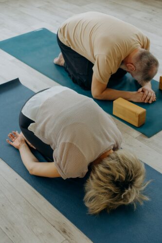 Two people doing yoga and entering balasana