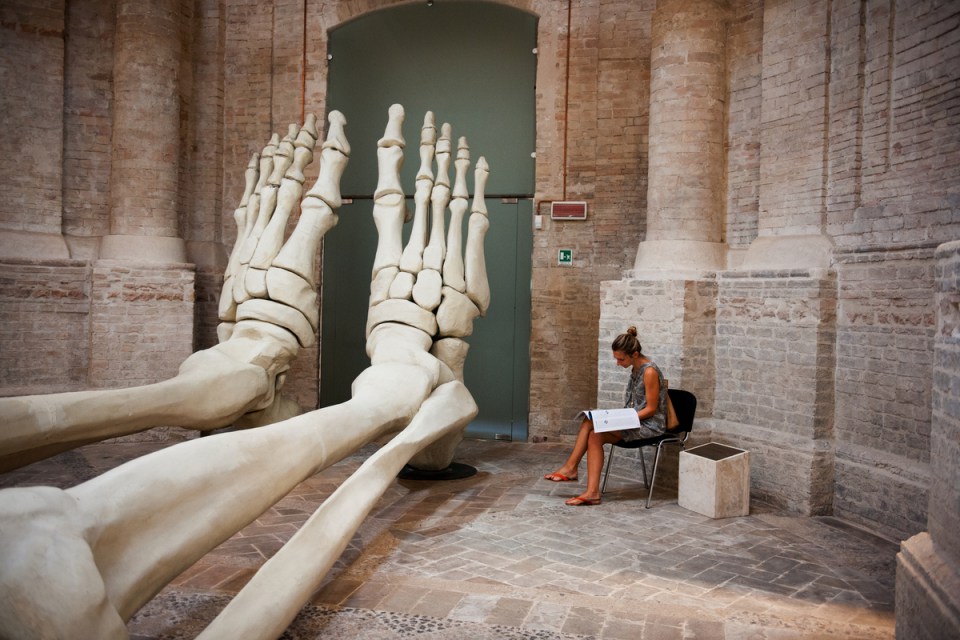 _2SM5531; Folingno, Umbria, Italy; 06/2012; Sculpture â??Calamita Cosmicaâ? by Gino Dedomincis; Ss.ma Annunziata e Trinita, ITALY-10406. A woman sits in front of a large sculpture. retouched_kate