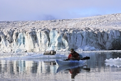 posserende skæg-sæl på isflage foran Esmarkbreen i Ymerbugten på Svalbard mens naturguide Roald Lande glider forbi i kajak.