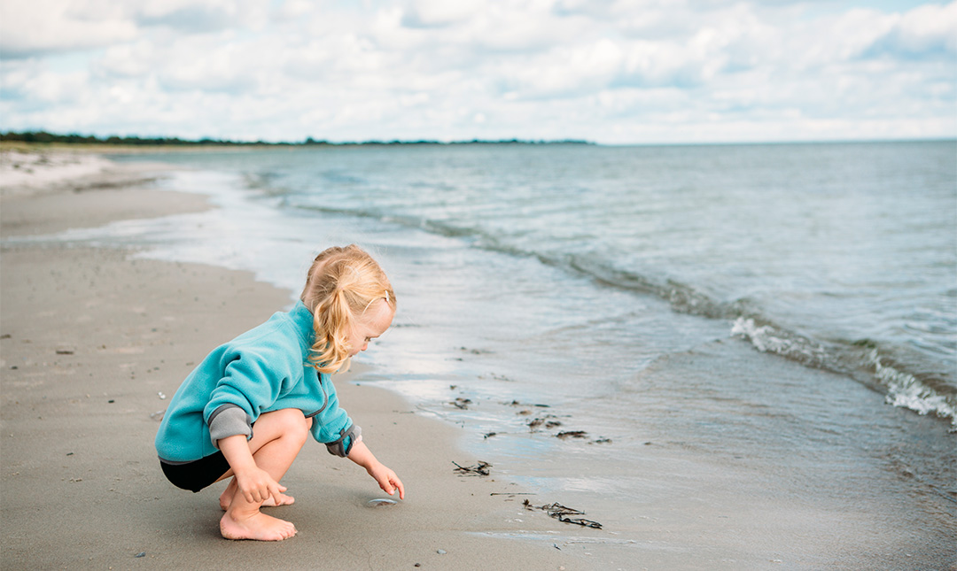 Girl on a beach picking up a jellyfish