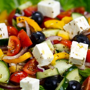 Fresh Close Up Vegetable Greek Salad with Feta cheese, black olives, cherry tomatoes, yellow pepper, red onion, cucumber. On wooden table