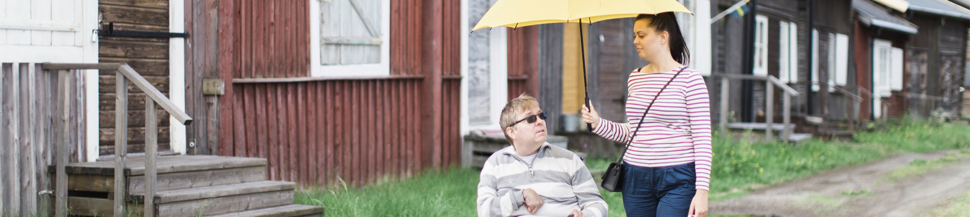 brukare i rullstol tillsammans med personlig assistent som håller paraply