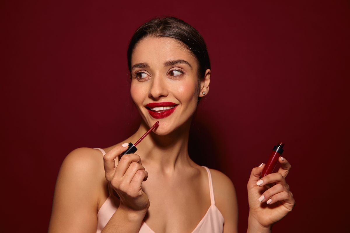 Woman applying Matte Red Lipstick and holding liquid lipstick bottle in other hand