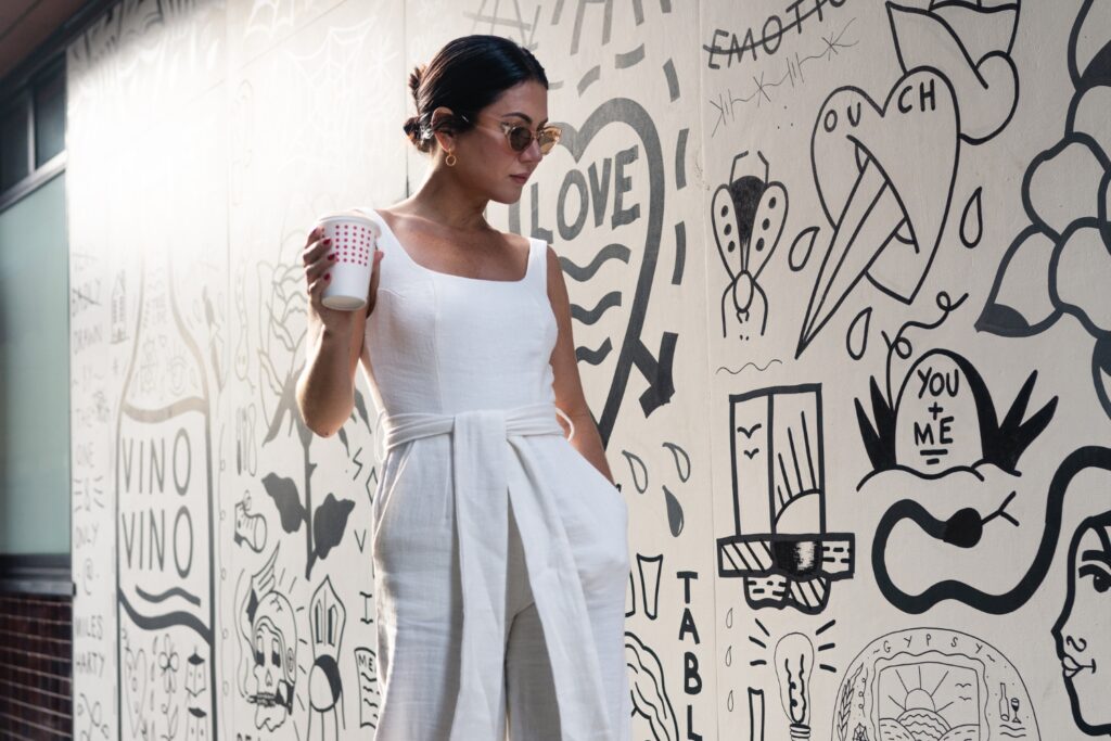 Woman in white dress holding coffee paper cup in her hand and looking at a word cloud wall