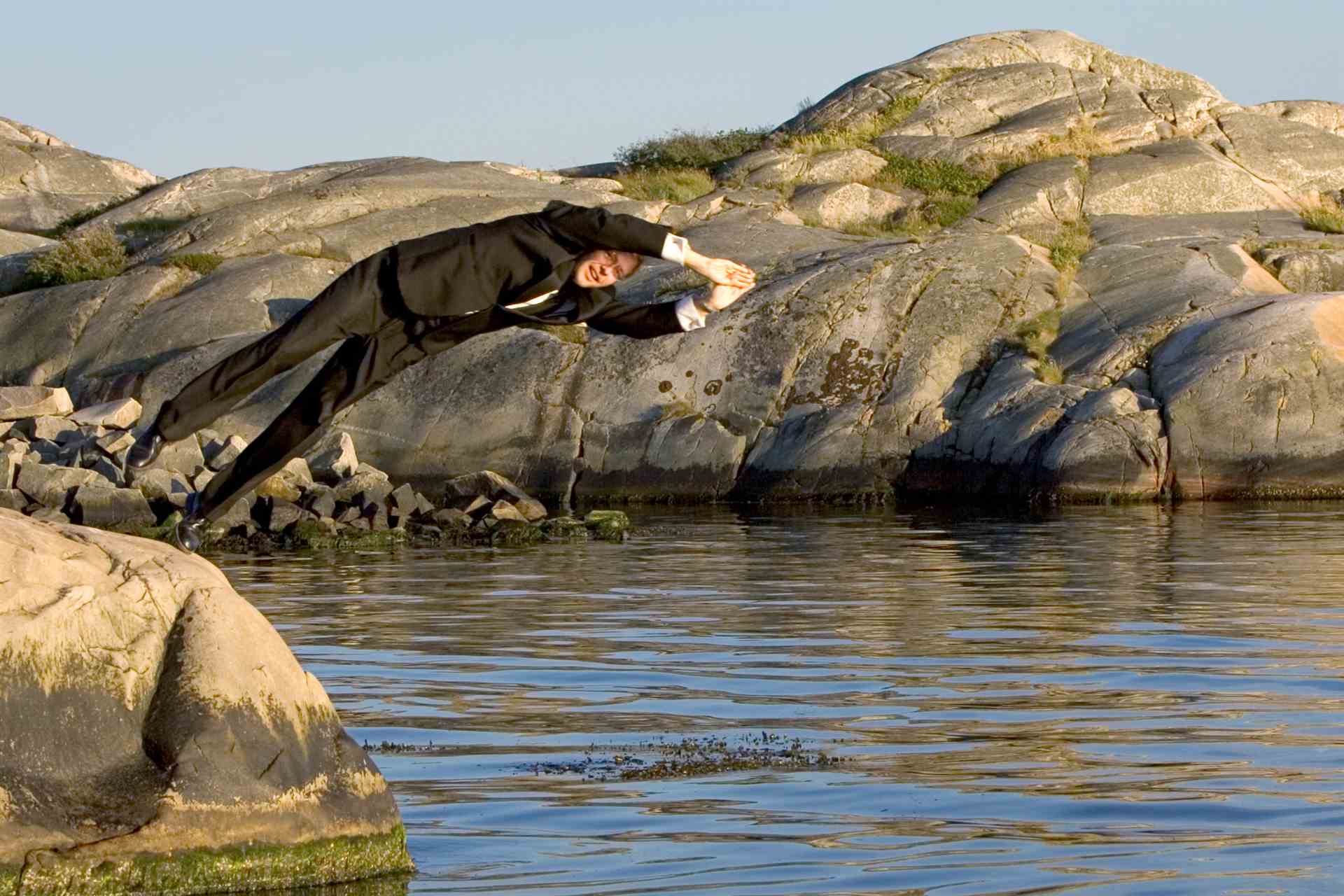 Bland klipporna i Göteborg dyker en man ned i vattnet med smoking.