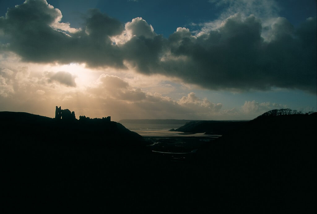 Sun breaking through the clouds over Pennard Castle near Three Cliffs Bay