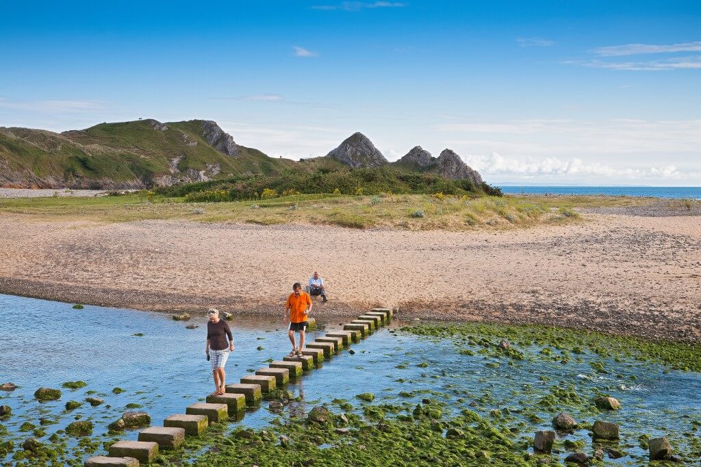 People walking across the stepping stones at Three Cliffs Bay