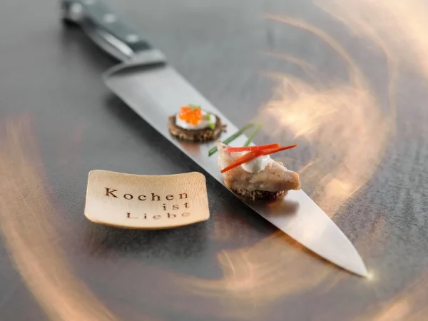 Amuse gueulle artfully arranged atop a kitchen knife, with a note on the side saying “Kochen ist Liebe,” which translates to “Love to cook.”