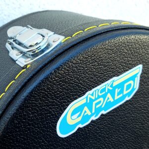 A logo sticker with the words 'Nick Capaldi' written in yellow with a light blue shadow. Sticker is placed on a black guitar case.