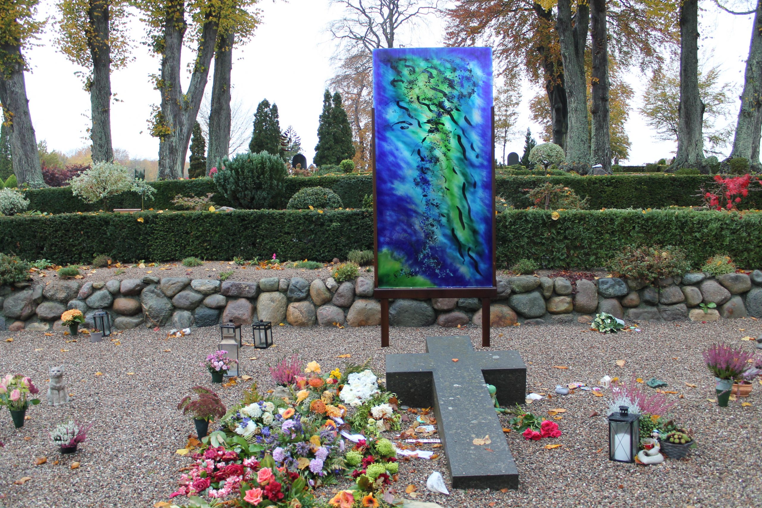 Grav monument i glas. En glasplade i grøn/blå nuancer på Herlufsh