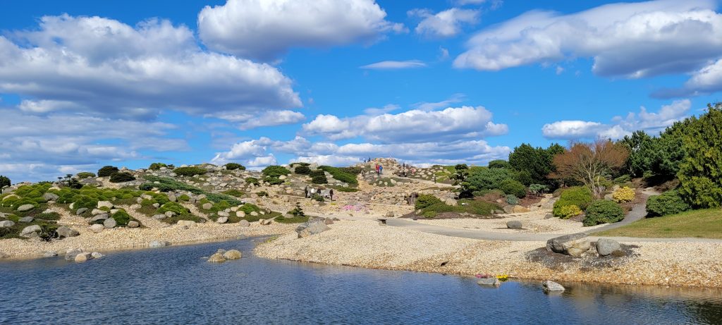 Findlingspark Nochten, Blick auf einen angelegten See mit "Felslandschaft" im Hintergrund, dazwischen erwacht die Natur langsam