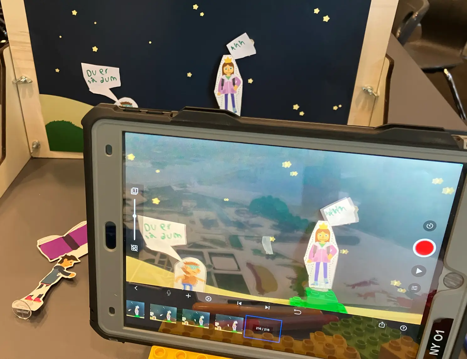 Tablet viser animation med udskårne figurer og talebobler foran nattebaggrund.