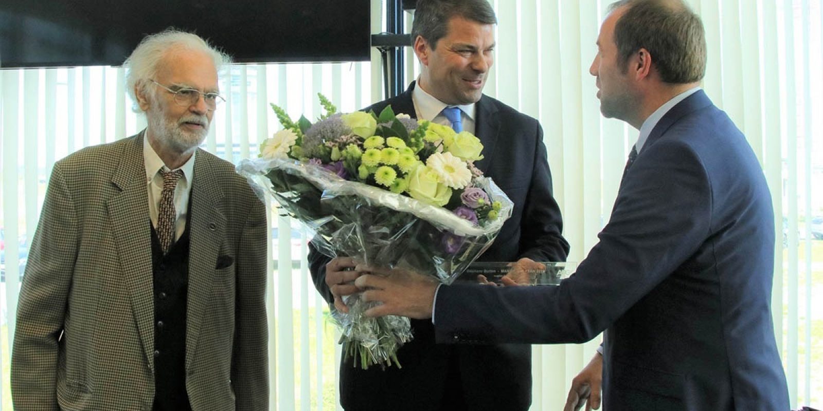 Le nouveau président de l’APC, Steven De Craene, assisté  du président d’honneur Patrick Anspach, remet le trophée MOTY à Stéphane Burton, CEO de Sabena Aerospace. (photo APC)