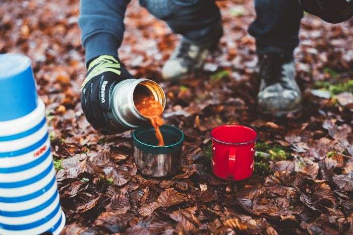 person in hiking gloves camping and pouring coffee