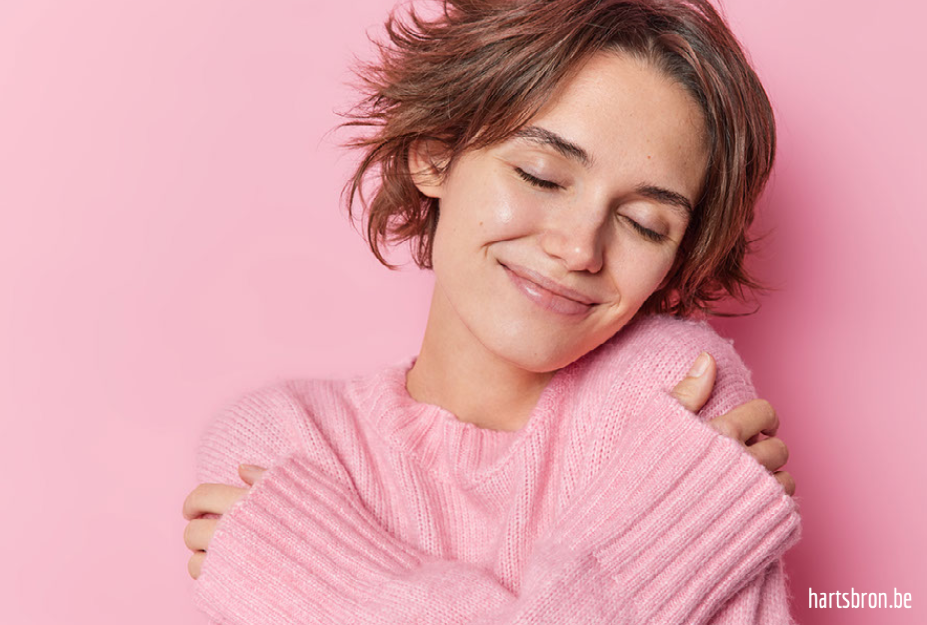 Joy as a signpost-1-2 glimlachende jonge vrouw omarmt zichzelf met de ogen gesloten, zachte roze trui