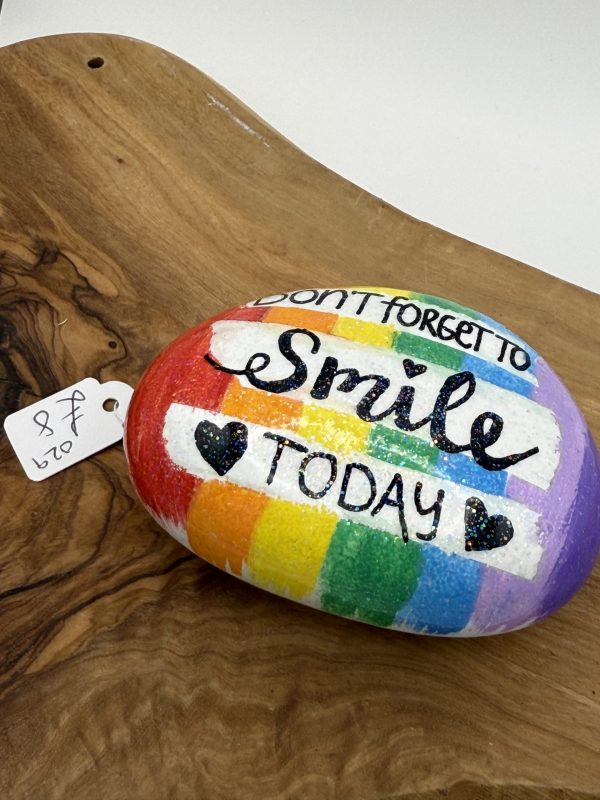 Vibrant Painted Rock with Inspiring Message: Dont Forget to Smile Today Decorated with Rainbow Stripes and Black Hearts on a Wooden Surface. Available for $8.00.