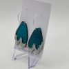 Discover stunning teal and silver glitter acrylic dangle earrings shaped like leaves, elegantly displayed on a clear stand against a minimalist background. These eye-catching earrings hang from sleek circular silver hoops and come beautifully presented on a white card. Perfect for adding sparkle to any outfit!.